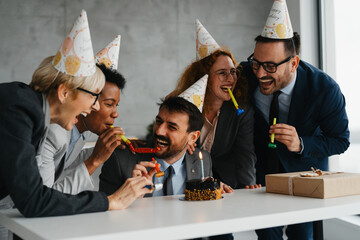 Happy colleagues celebrating a coworker's birthday in a modern office with a delicious cake on the desk