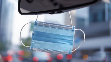 Disposable medical face mask hanging from a car rearview mirror highlighting personal safety and hygiene during daily urban travel
