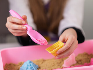 Child playing with kinetic sand, scooping sand into a mold to create various shapes, close-up of hands in frame