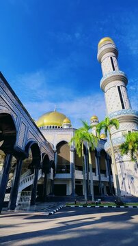 The golden dome and building of the Jamil Asra Hassan Al-Bolkiah Mosque in Bandar Seri Bagawan, Brunei Darussalam, are framed by tropical palm trees on a sunny day. Asia. 4К
