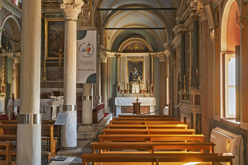  the Cathedral of Saint George in Ano Syros showcasing  columns, arches, and a vaulted ceiling with intricate artwork. The central altar is draped in white cloth and framed by golden columns 