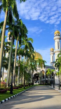 The golden dome and building of the Jamil Asra Hassan Al-Bolkiah Mosque in Bandar Seri Bagawan, Brunei Darussalam, are framed by tropical palm trees on a sunny day. Asia. 4К