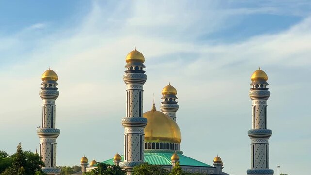 The golden dome and building of the Jamil Asra Hassan Al-Bolkiah Mosque in Bandar Seri Bagawan, Brunei Darussalam, are framed by tropical palm trees on a sunny day. Asia. 4К