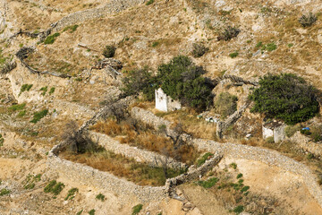 Historic hillside scene in Ano Syros, Greece, featuring terraced stone walls and a mix of preserved and ruined structures