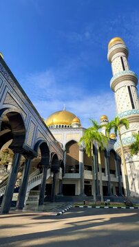 The golden dome and building of the Jamil Asra Hassan Al-Bolkiah Mosque in Bandar Seri Bagawan, Brunei Darussalam, are framed by tropical palm trees on a sunny day. Asia. 4К