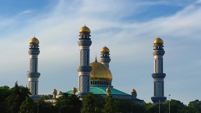 The golden dome and building of the Jamil Asra Hassan Al-Bolkiah Mosque in Bandar Seri Bagawan, Brunei Darussalam, are framed by tropical palm trees on a sunny day. Asia. 4К