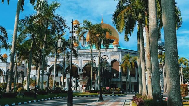The golden dome and building of the Jamil Asra Hassan Al-Bolkiah Mosque in Bandar Seri Bagawan, Brunei Darussalam, are framed by tropical palm trees on a sunny day. Asia. 4К