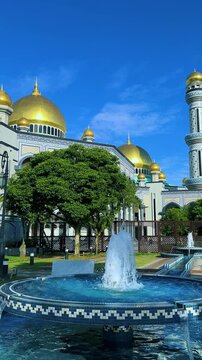 The golden dome and building of the Jamil Asra Hassan Al-Bolkiah Mosque in Bandar Seri Bagawan, Brunei Darussalam, are framed by tropical palm trees on a sunny day. Asia. 4К