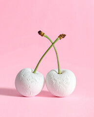Two white frozen cherries against a pastel pink background, creative fruit concept