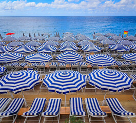 Pebble beach along Promenade des Anglais with beach umbrellas and chairs with the turquoise water of the Mediterranean Sea in Nice, Cote d'Azur France