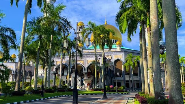 The golden dome and building of the Jamil Asra Hassan Al-Bolkiah Mosque in Bandar Seri Bagawan, Brunei Darussalam, are framed by tropical palm trees on a sunny day. Asia. 4К