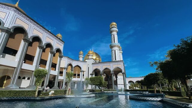 The golden dome and building of the Jamil Asra Hassan Al-Bolkiah Mosque in Bandar Seri Bagawan, Brunei Darussalam, are framed by tropical palm trees on a sunny day. Asia. 4К