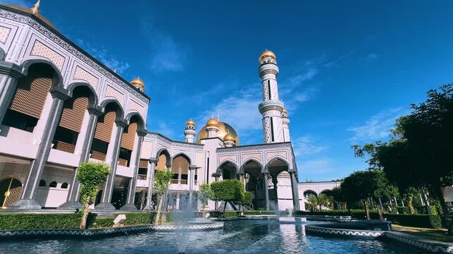 The golden dome and building of the Jamil Asra Hassan Al-Bolkiah Mosque in Bandar Seri Bagawan, Brunei Darussalam, are framed by tropical palm trees on a sunny day. Asia. 4К