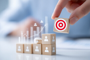 A hand places a target block atop a stack of blocks with figures, symbolizing effective leadership, strategy, and team achievement in a business setting focused on growth