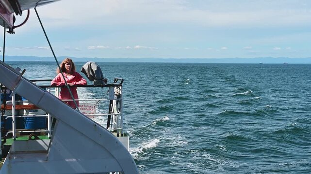 On a tranquil day at sea near Sakhalin Island, a girl joyfully stands on a vessel, her hair dancing in the wind as waves gently lap against the hull, creating a serene atmosphere.