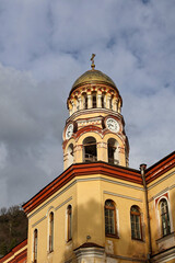Fototapeta premium New Athos Monastery photographed on a sunny day. Close-up of the bell tower framed by palm trees under a blue sky, highlighting Orthodox architecture, historic heritage and a scenic Abkhazia landmark.