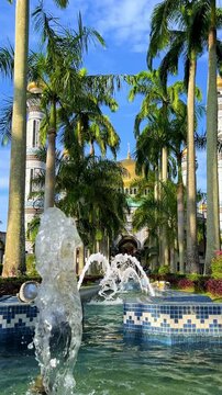 The golden dome and building of the Jamil Asra Hassan Al-Bolkiah Mosque in Bandar Seri Bagawan, Brunei Darussalam, are framed by tropical palm trees on a sunny day. Asia. 4К