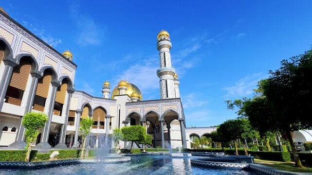The golden dome and building of the Jamil Asra Hassan Al-Bolkiah Mosque in Bandar Seri Bagawan, Brunei Darussalam, are framed by tropical palm trees on a sunny day. Asia. 4К