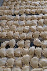 Obraz premium Cluster of handmade dumplings with pleated edges on paper towel, selective focus highlights texture amid cooking at home scene with scattered dough in background