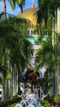 The golden dome and building of the Jamil Asra Hassan Al-Bolkiah Mosque in Bandar Seri Bagawan, Brunei Darussalam, are framed by tropical palm trees on a sunny day. Asia. 4К