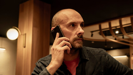 A mature businessman sitting at a cafe table, focused on his mobile phone. He is checking emails or working remotely in a professional yet relaxed urban environment.