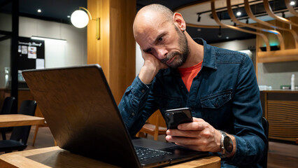 A mature professional man sitting at a cafe table, working on a laptop computer. He is focused on his tasks, representing remote work.