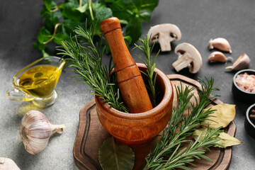 Wooden mortar with different herbs and fresh mushrooms on grunge background, closeup