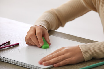 Child erasing drawing in notebook at table, closeup