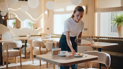 Fototapeta premium Cafe waitress cleaning table taking dishes after client. Girl staff working