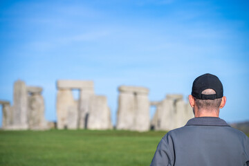 Selective focus on a man as he views ancient stone formation at Stonehenge in England during daytime with clear sky