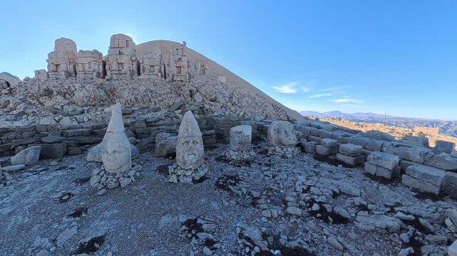 A sweeping view across the rocky summit of Mount Nemrut (Nemrut Dağı) in Turkey reveals the massive, weathered stone heads of ancient deities and the iconic artificial tumulus burial mound under a cle