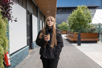 Woman walking outdoors with takeaway coffee cup, reflecting on urban lifestyle and modern city architecture