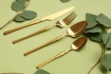 Stylish golden cutlery and eucalyptus branches on green background, closeup