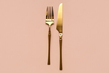 Stylish golden fork and knife on beige background