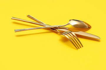 Stylish golden cutlery on yellow background, closeup