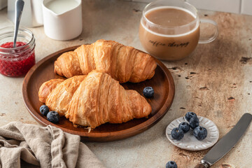 Delicious breakfast with croissants on wooden tray and coffee on white kitchen table background close up