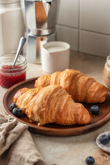 Delicious breakfast with croissants on wooden tray and coffee on white kitchen table background close up