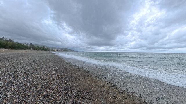 Small waves crashing against the shore of the Black Sea on a pebbly beach near Hopa, Turkey under a dense layer of grey storm clouds
