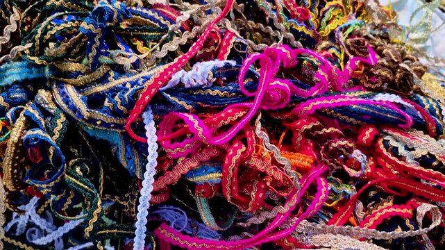 A close-up of a tangled assortment of colorful threads, laces and cords piled together, showing varied textures and bright hues commonly used for crafts, jewelry making, or decorative tying.