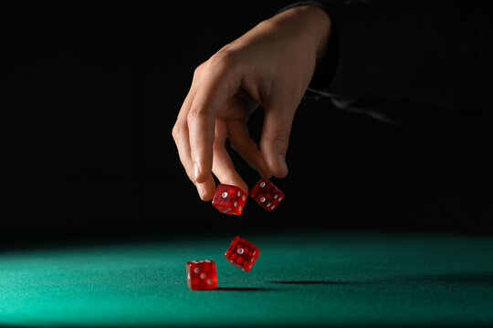 Male hand throwing red game dices on green table against black background