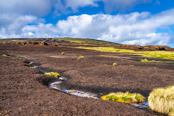 Eroded peatland landscape with exposed dark soil and isolated peat ‘islands’ under a bright...
