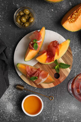Board of fresh melon pieces with delicious prosciutto and mint leaves on dark background