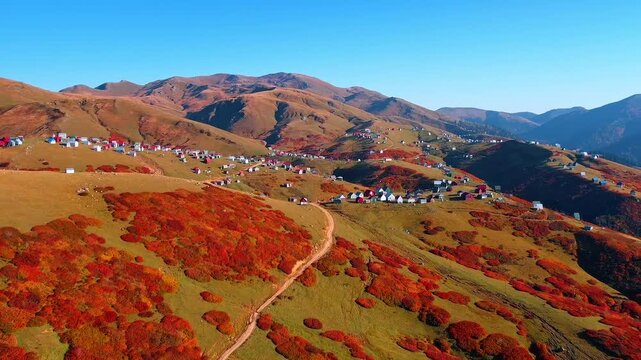 Beautiful slopes of high rocks are covered with stunning colorful vegetation. Approaching the village scattered in the picturesque mountains. Aerial view.