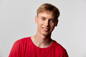 Smiling man wearing a red t-shirt in a bright studio with soft lighting and a clean grey background, casual and approachable vibe, suitable for lifestyle, fashion, or corporate culture concepts.