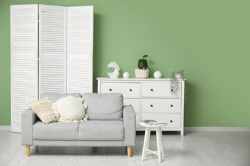 Obraz premium Interior of modern room with folding screen, armchair and sofa near green wall