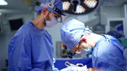 Two neurosurgeons in blue uniforms cooperate at operation. Chief surgeon applies diverse tools at work.
