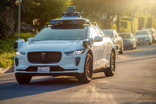 LOS ANGELES, CA - May 2, 2025: Self-driving  Waymo driverless taxi cab driving along sunny city street in warm glowing sunset light.