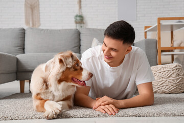 Young man with cute Australian Shepherd dog lying on carpet in living room
