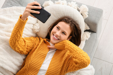 Pretty young woman taking selfie while lying on sofa at home