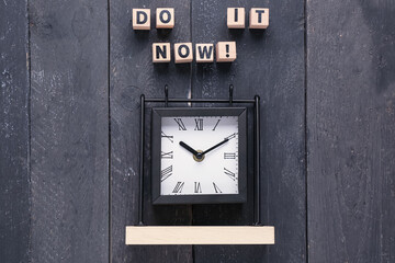 Cubes with text DO IT NOW and alarm clock on black wooden background. Top view